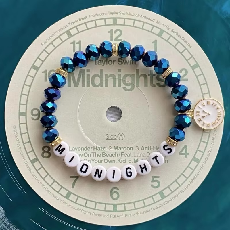 Blue beaded bracelet with white beads spelling 'Midnights and a clock charm.