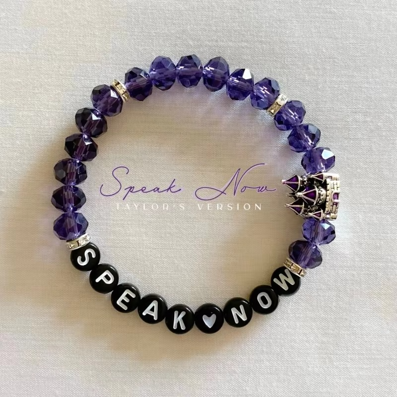Purple beaded bracelet with 'Speak Now' black beads and a castle charm.