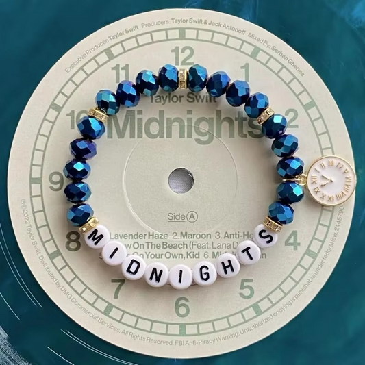 Blue beaded bracelet with white beads spelling 'Midnights and a clock charm.