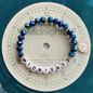 Blue beaded bracelet with white beads spelling 'Midnights and a clock charm.